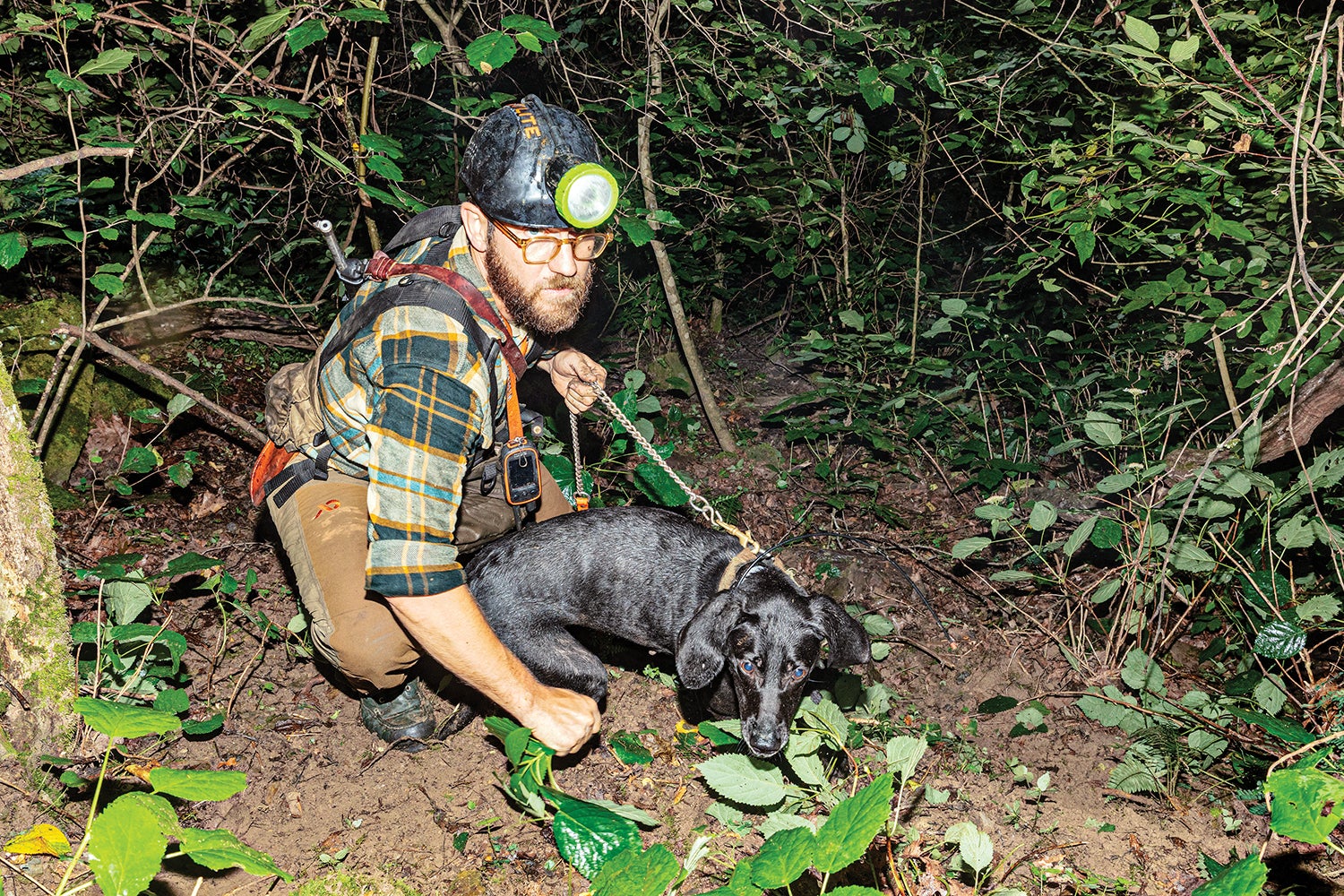 hunter wearing headlamp crouches and holds dog by leash