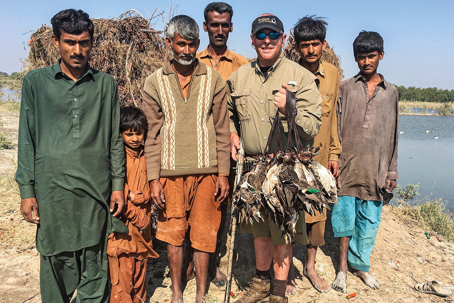 american duck hunter with many birds poses with guide staff in pakistan